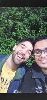 Two friends enjoying laughter in nature with a green backdrop.