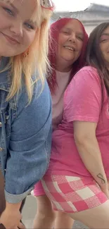 Three friends pose happily in pink on a sunny day.