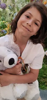 Smiling child holding teddy bear in vibrant garden.