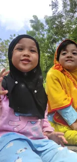 Two smiling children outdoors in colorful outfits with nature background.