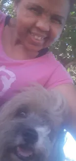 Smiling person with a dog outdoors in a pink shirt.