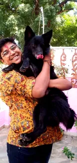 Person joyfully holding a black dog outdoors with vibrant greenery.