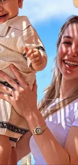 Mother holding child under blue sky, smiling brightly.