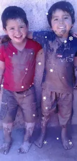 Two joyful children covered in mud, smiling warmly against a beige wall.