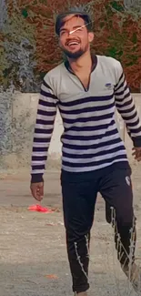 Man smiling outdoors in striped shirt, joyful scene.