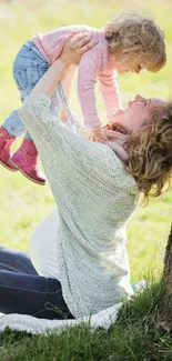 Mother and child joyfully playing outdoors under a tree.