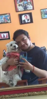 A joyful selfie with a dog in front of an orange wall mirror.