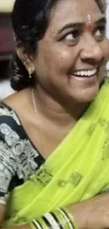 Smiling woman wearing a green saree with traditional patterns.