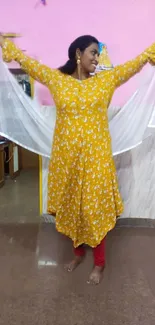 Woman in a yellow floral dress joyfully posing indoors.