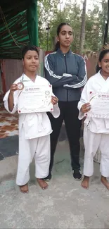 Two young karate students holding certificates with instructor.