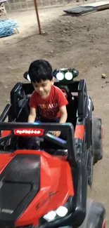 Kid enjoying a ride in a red toy jeep on a sandy surface at night.