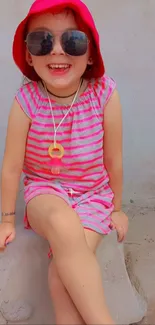 Smiling child in vibrant pink outfit and sunglasses on a sunny day.