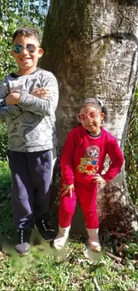 Two kids posing by a tree in a vibrant outdoor setting.