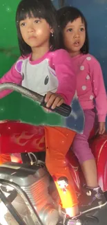 Two kids enjoy a ride on a bright red toy motorcycle against a colorful backdrop.