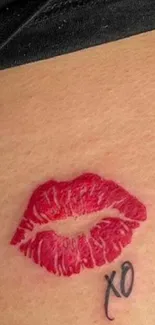 Red lipstick kiss tattoo with 'XO' on skin close-up.