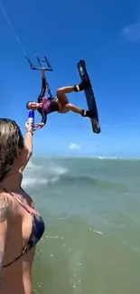 Kitesurfer catching air over the ocean with a vibrant blue sky background.