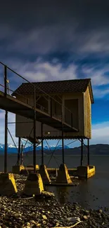 Lakeside cabin under dusky blue sky with rocky shoreline.