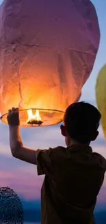 Boy holding lantern under a colorful evening sky.