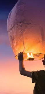 Silhouette of person releasing glowing lantern into sunset sky.