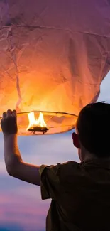 Boy releasing a glowing lantern into the evening sky.