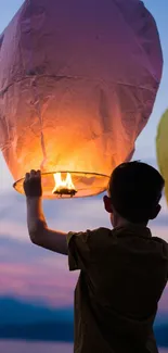 A child releases a glowing lantern into the colorful evening sky.