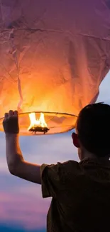 Child releases glowing lantern at sunset with vibrant orange sky.