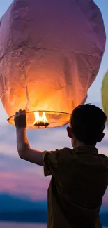 Child releases glowing lanterns under colorful sunset sky.