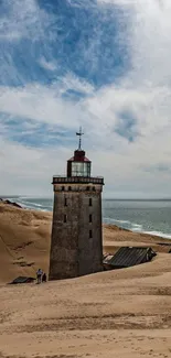 Lighthouse standing on sandy coastline under a blue sky.