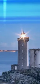 Lighthouse glowing at dusk with ocean backdrop.