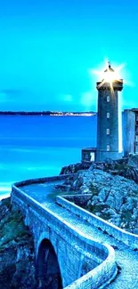 A lighthouse on a rocky coast, glowing at dusk with a vivid blue sky.