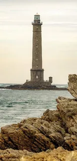 Lighthouse standing tall by rocky seashore with a calm sea.