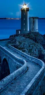 Lighthouse illuminated at dusk on a rocky shore with a winding stone path.