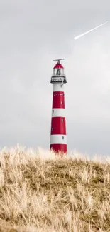 Lighthouse in grassy landscape under cloudy sky with a shooting star.