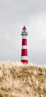 Red and white lighthouse amidst dunes under a cloudy sky.