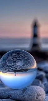 Glass sphere reflecting lighthouse at sunset on pebble beach.