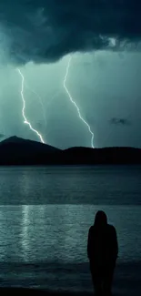 Silhouette by mountain lake with striking lightning in the night sky.