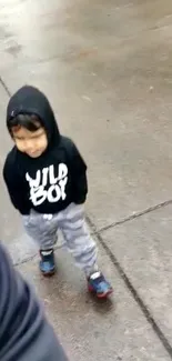 Young child in black hoodie walking on wet path.