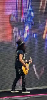 Guitarist performing on stage against a large screen.