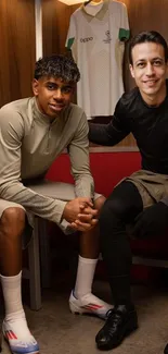 Two athletes in a locker room sitting on benches.