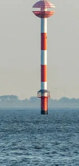 Lone red and white lighthouse in calm ocean.