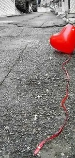 A red heart balloon on a gray, desolate street, creating a striking visual contrast.