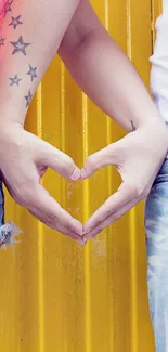 Couple making heart shape with hands on yellow background.