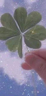 Four-leaf clover held against a starry sky with clouds.