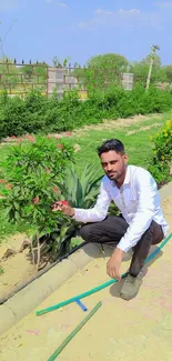 Man kneeling in a lush garden with vibrant green plants and a clear blue sky.