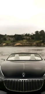 Luxury black car by a calm lakeside with trees in the background.