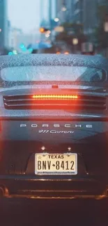 A luxury car in the rain with glowing taillights in a city setting.