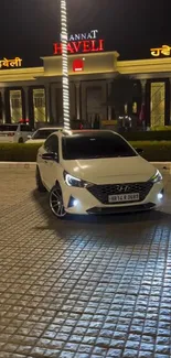 Luxury white car parked at night in front of a lit building.