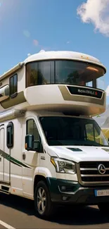 Luxury motorhome on scenic road with mountains and blue sky.