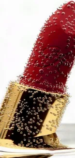 Red lipstick with bubbles in a gold casing on white background.