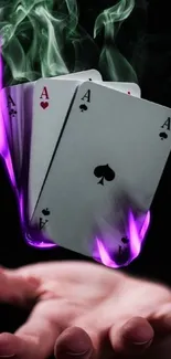 Floating playing cards with purple smoke and flames over a hand.